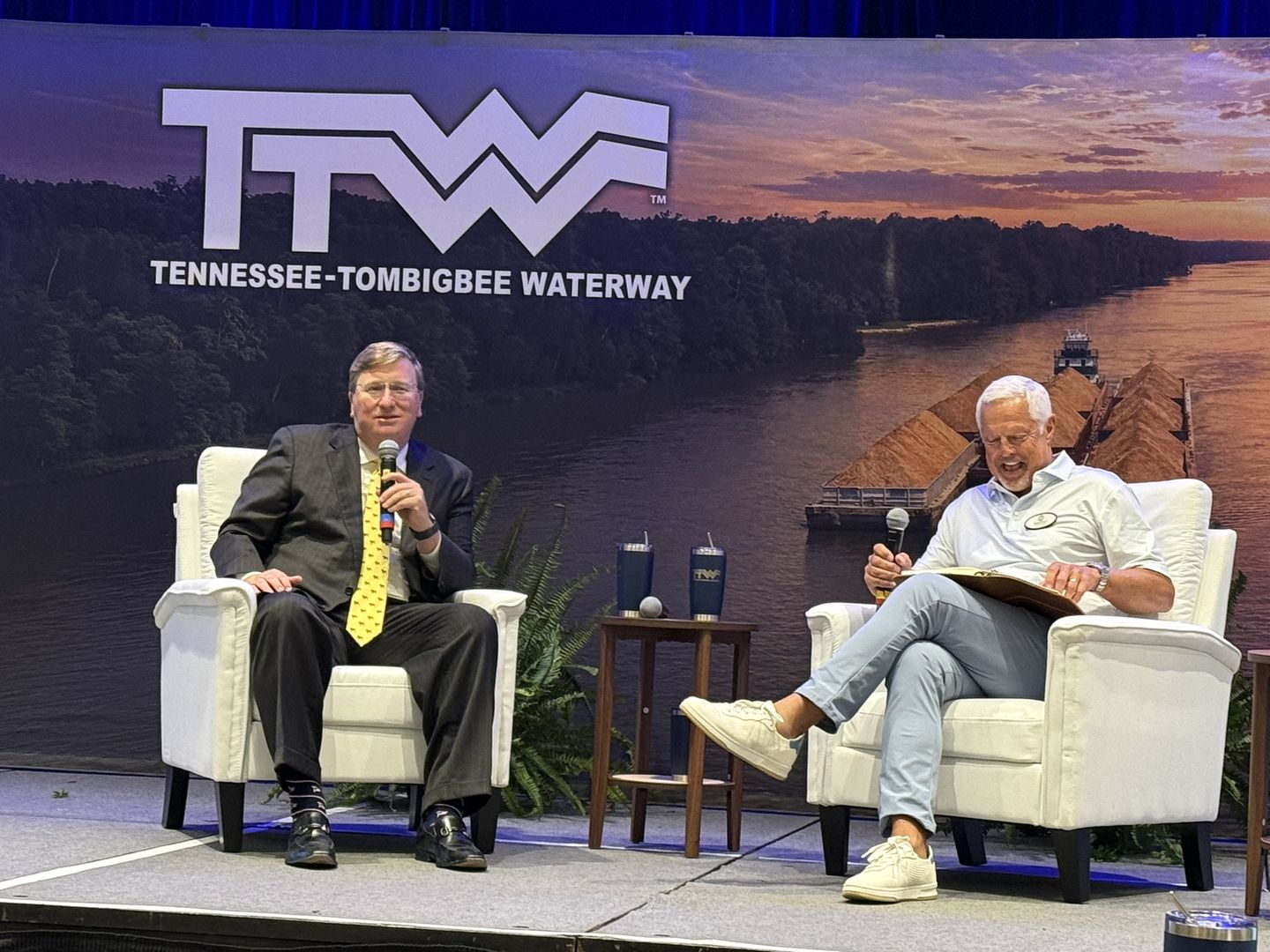 Two speakers in white armchairs talk on stage under the Tennessee-Tombigbee Waterway logo.