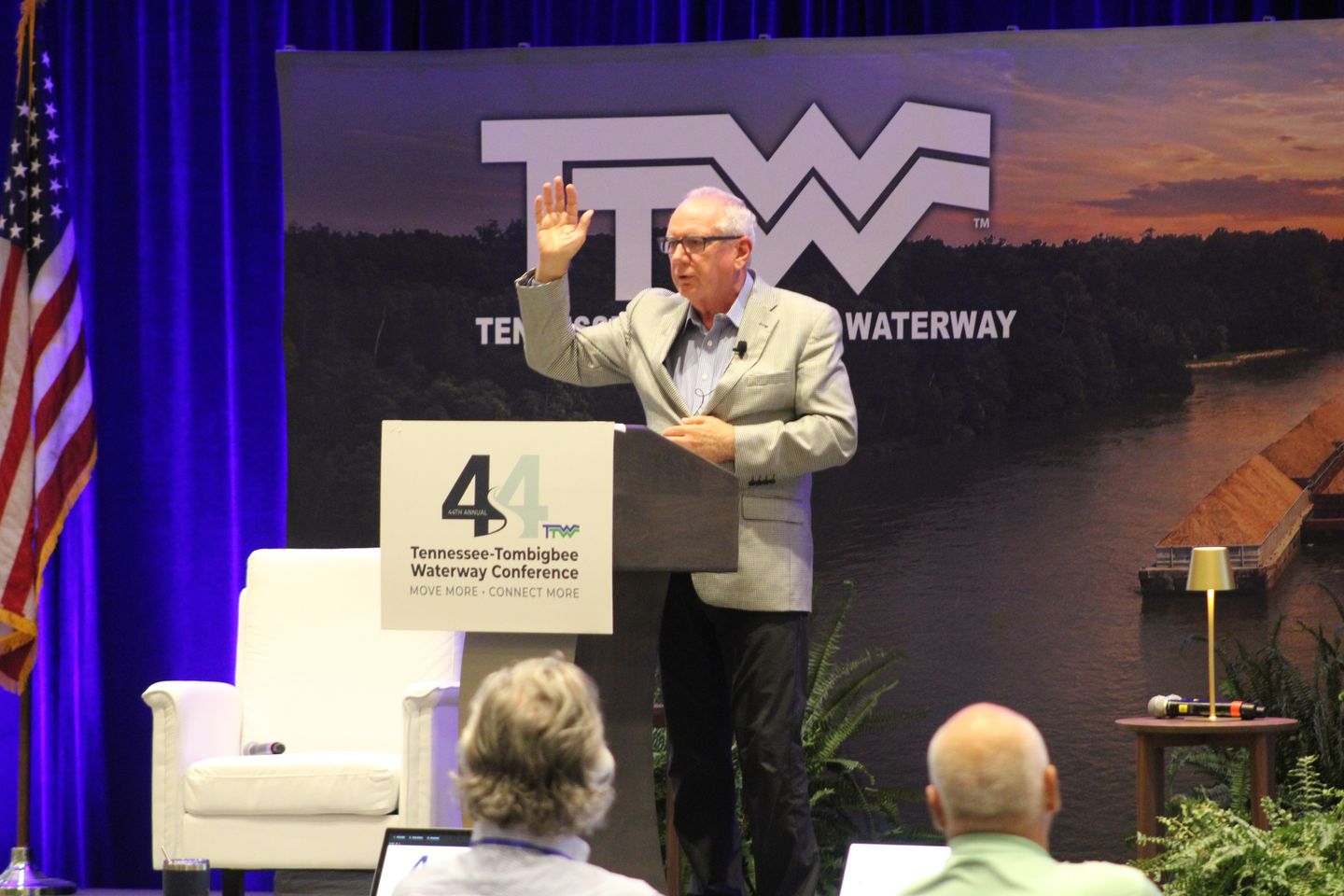 A speaker raises his hand from the podium on the main stage.