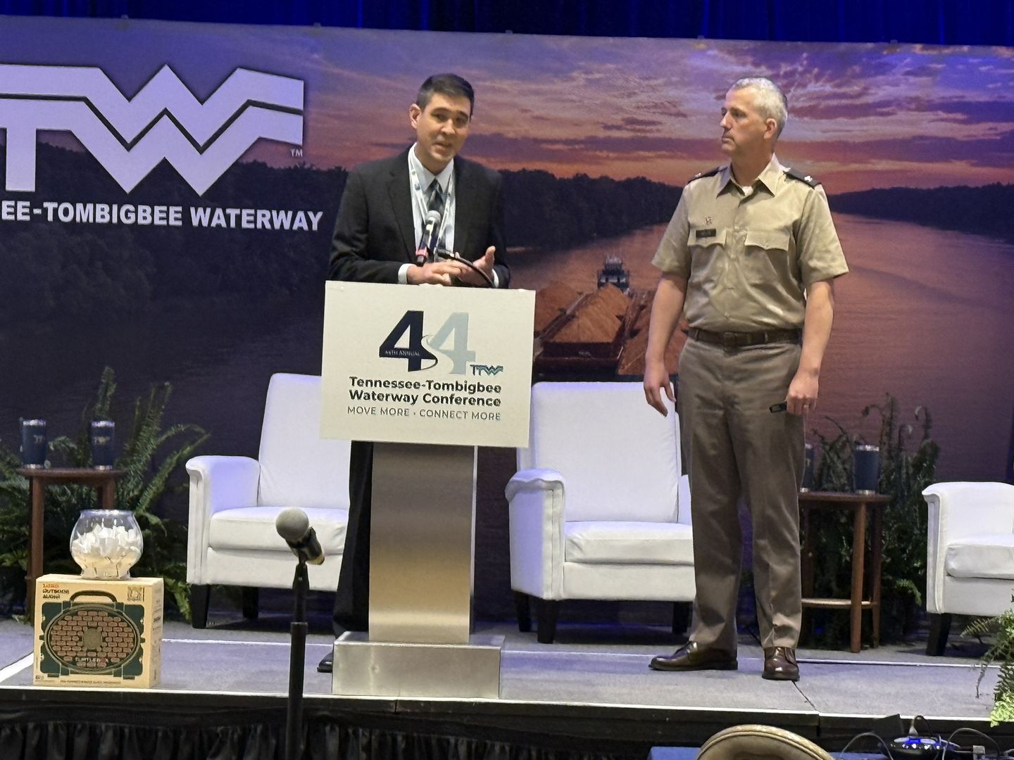 Two speakers on stage, one in Army uniform, under the Tennessee-Tombigbee Waterway logo.